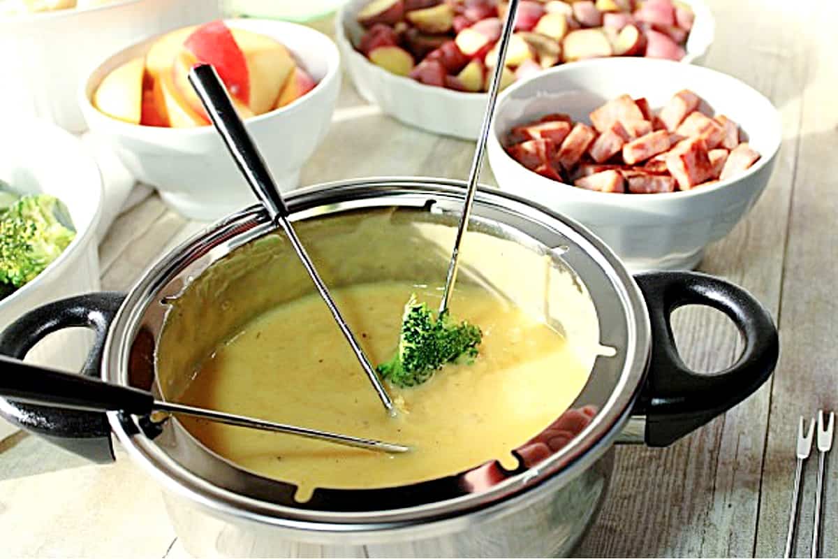 A broccoli floret on a fondue fork dipped in cheese sauce.