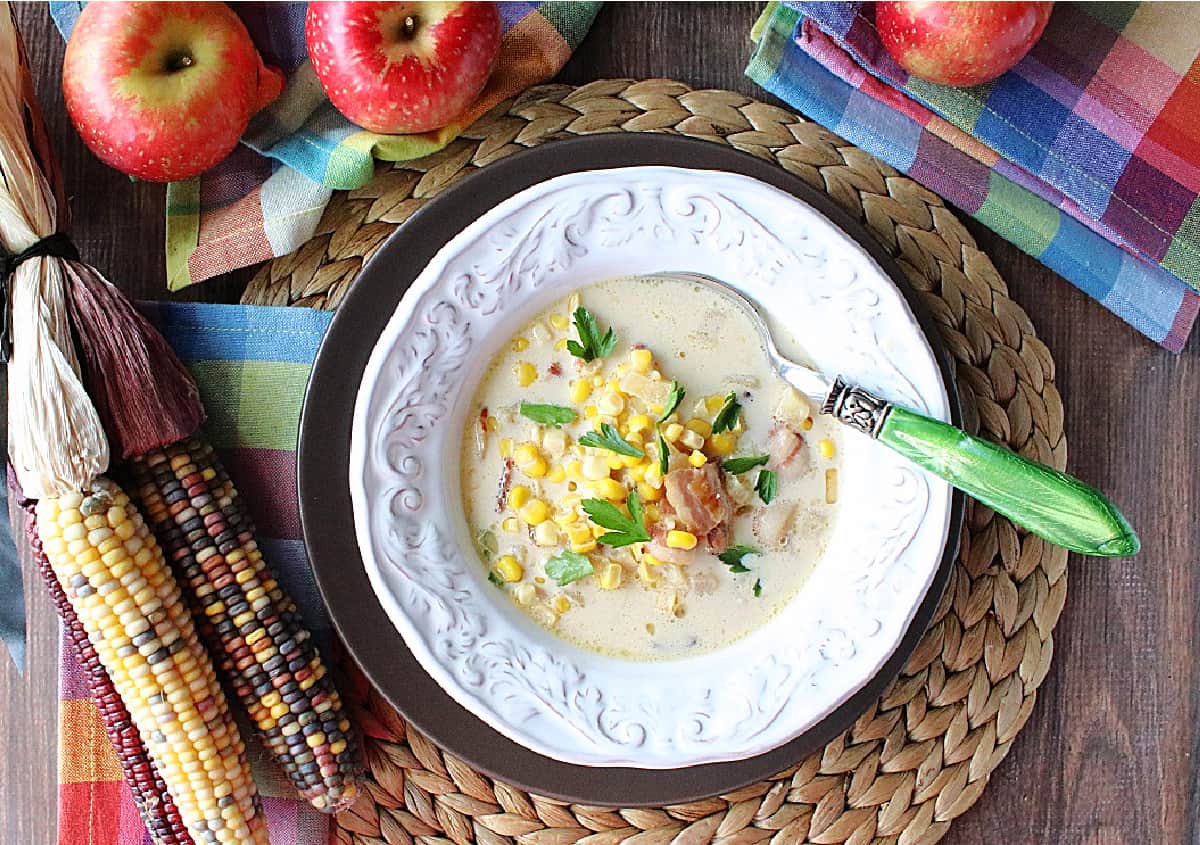 Apple Corn Chowder A pretty bowl of chowder with corn, bacon, and parsley along with apples in the background.