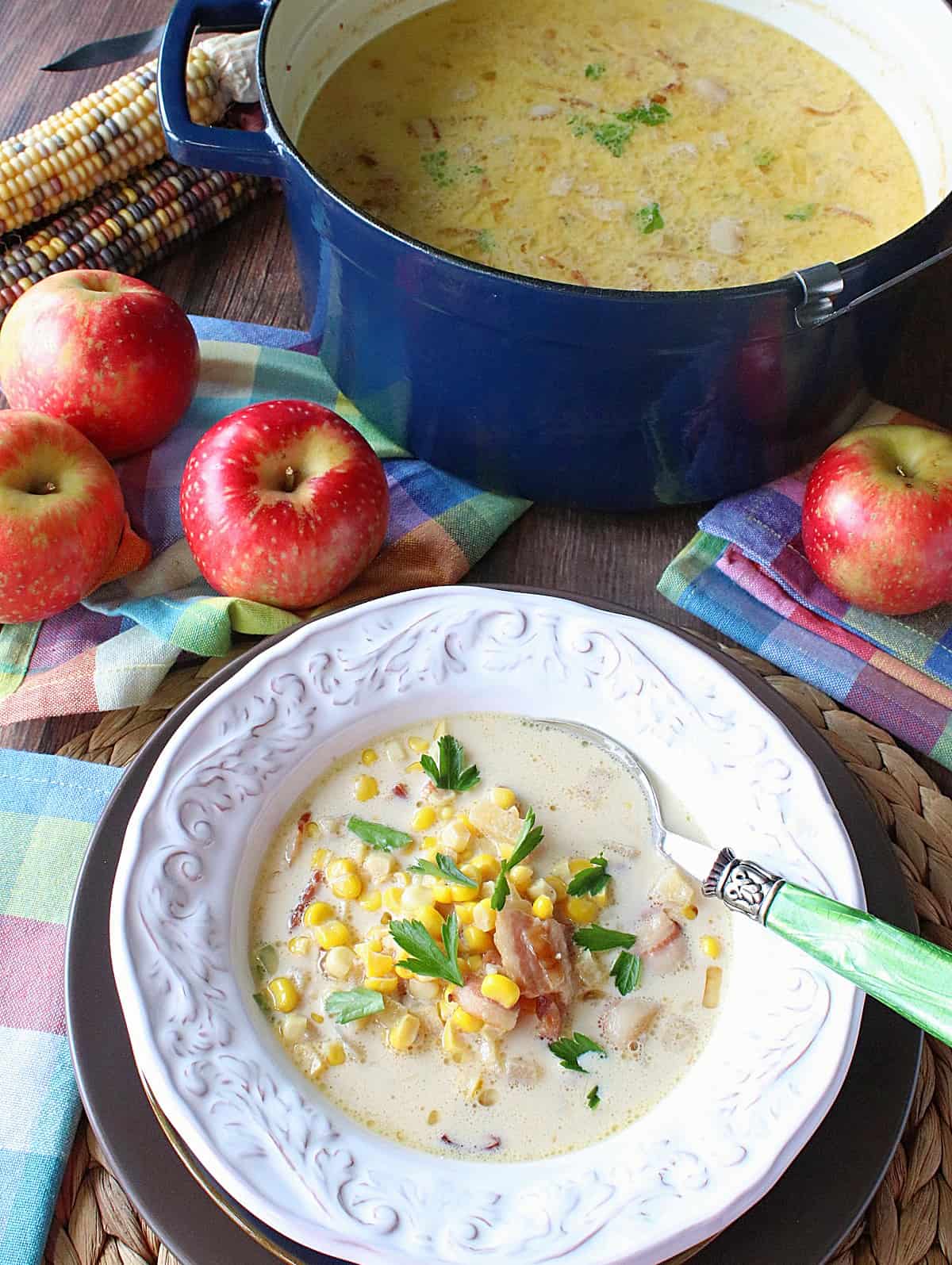 A large pot and a bowl with a serving of apple corn chowder with bacon.