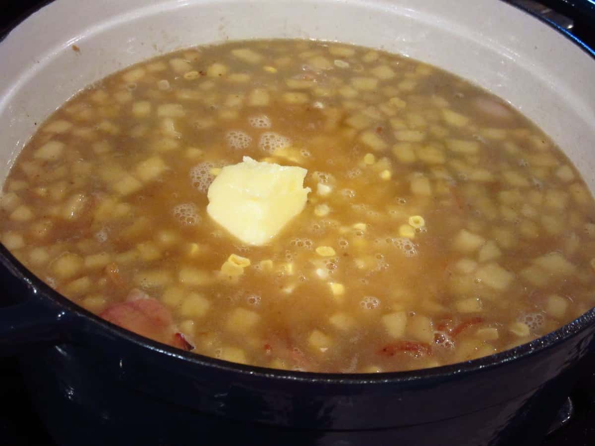A large pat of butter in a pot of apple corn chowder.