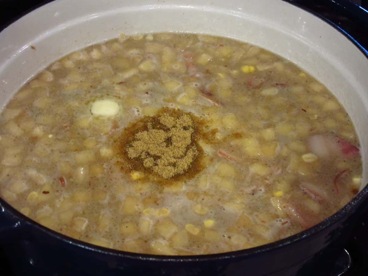Old bay seasoning in a pot of corn chowder with apples and bacon.