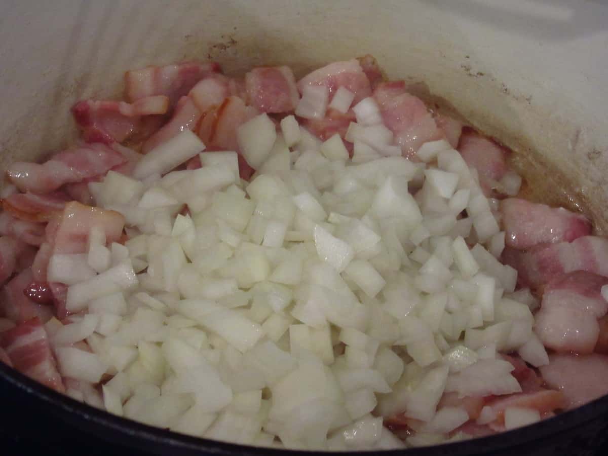 Bacon and chopped onion frying in a Dutch oven.