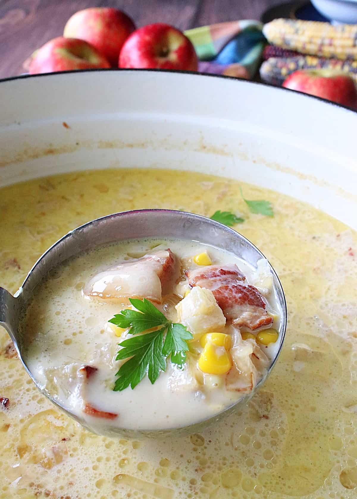A ladle spooning up a serving of corn chowder with a parsley leave on top.