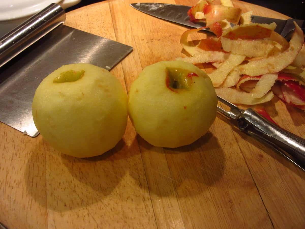 Two peeled apples on a cutting board.