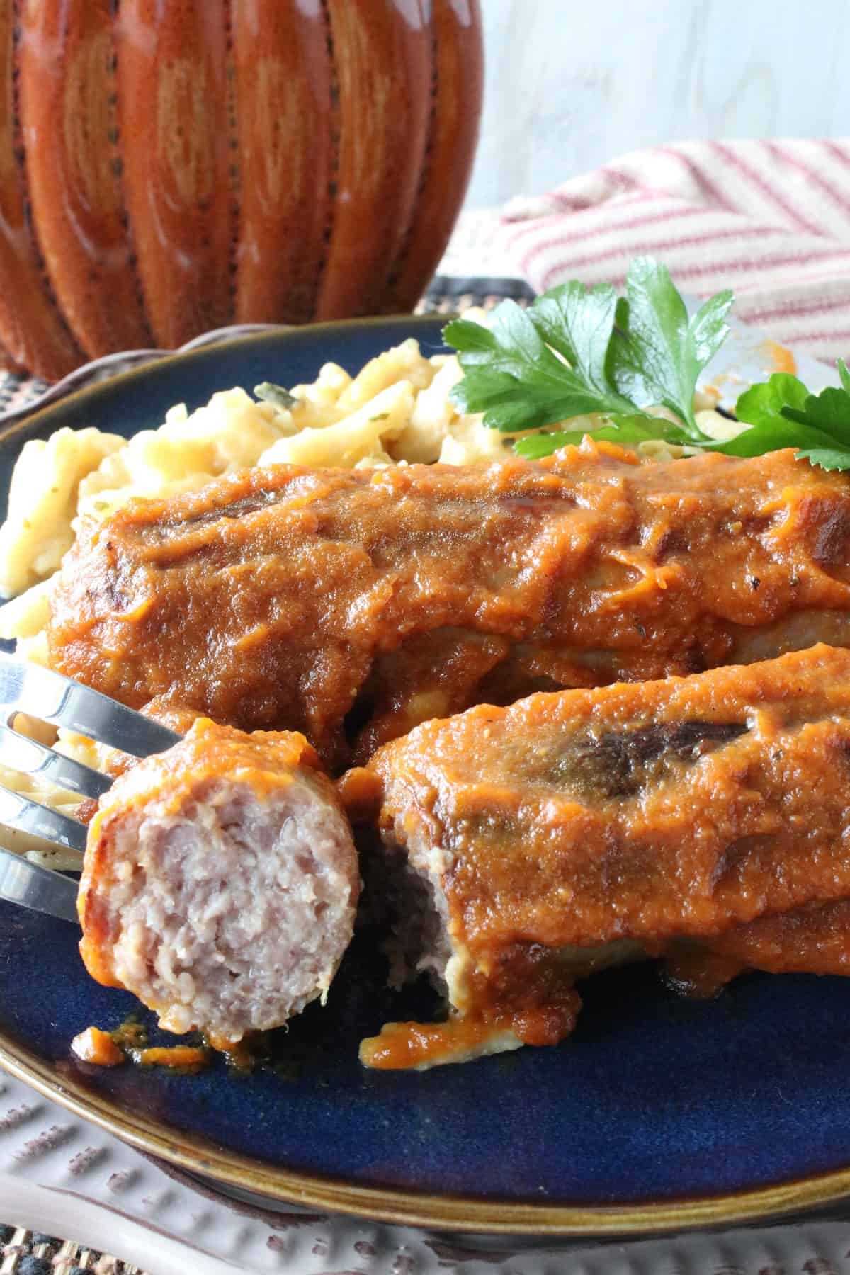 A fork with a bite of skillet bratwurst in pumpkin curry sauce on a blue plate.