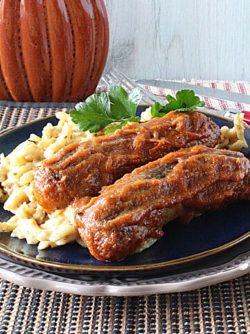 Two pumpkin curry bratwurst on a blue plate with a parsley garnish.