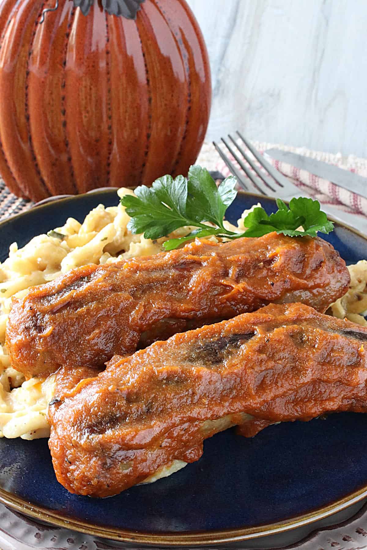 Two Pan Seared Bratwurst in Pumpkin Curry Sauce on a blue plate with spaetzle and parsley.