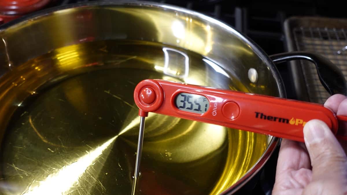An instant read thermometer in a skillet of hot oil.