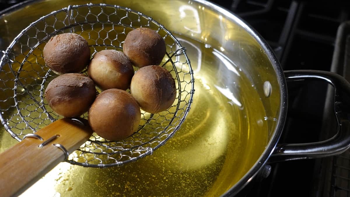 Apple cider donut holes being lifted from hot oil with a large slotted spider spatula.