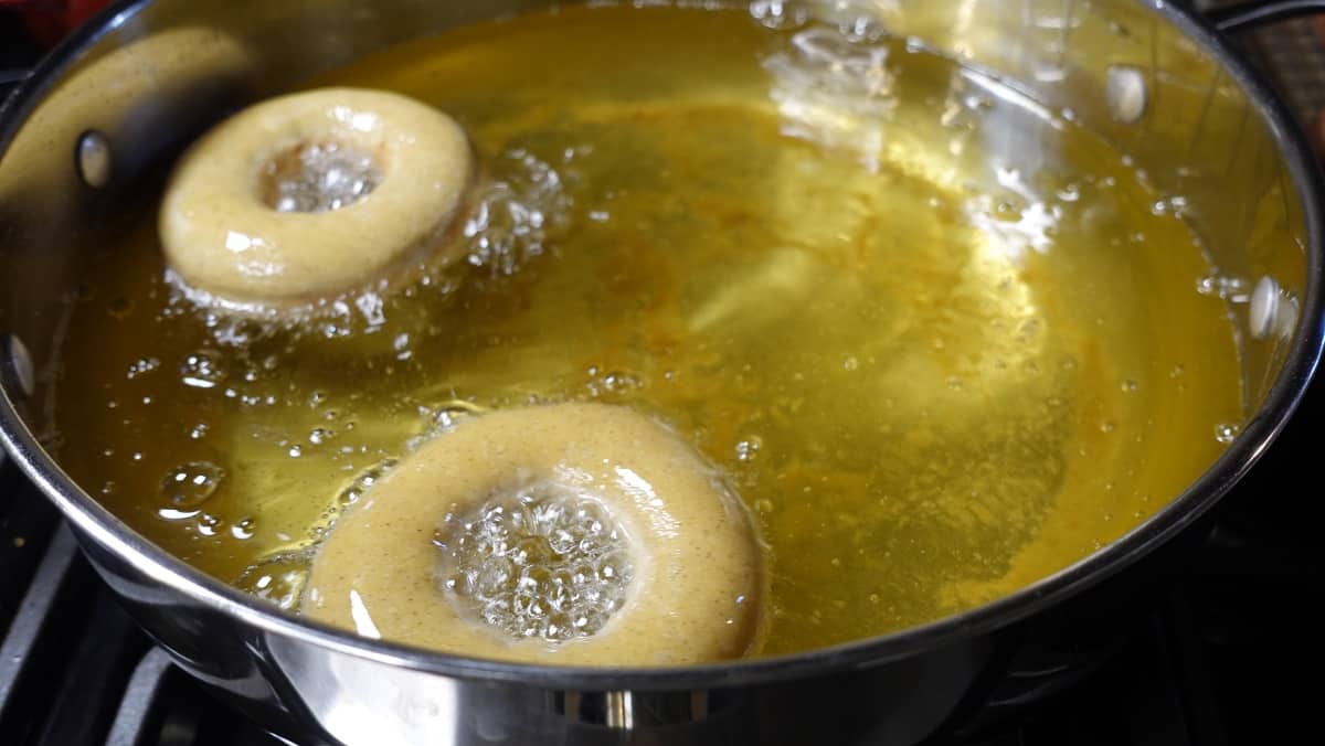 Apple cider yeast donuts frying in hot oil.