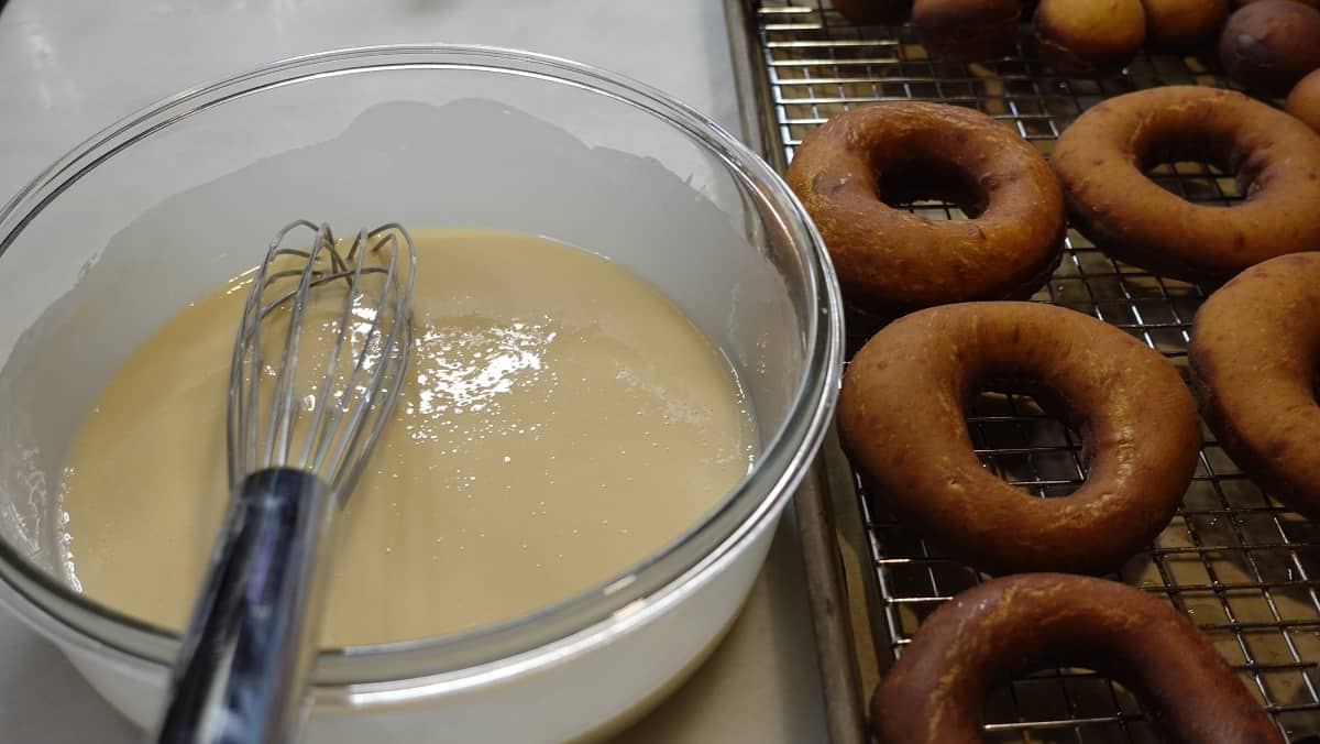 A glass bowl filled with apple cider glaze for yeast donuts.