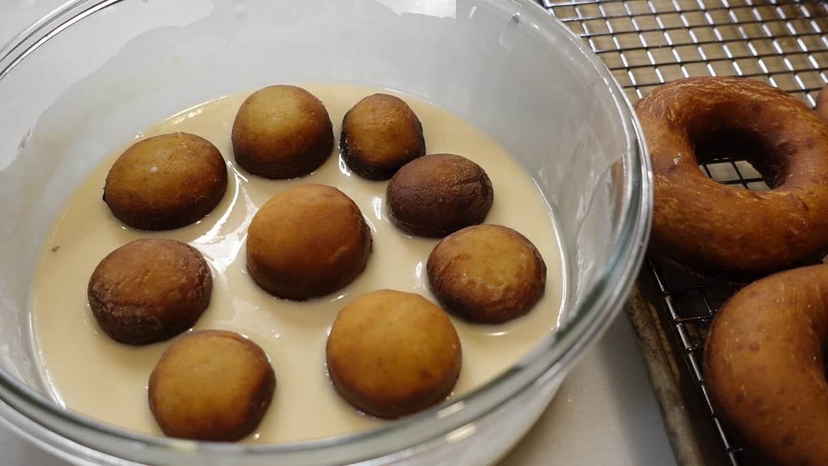 Fried Apple Cider Yeast Donuts being dipped into glaze.