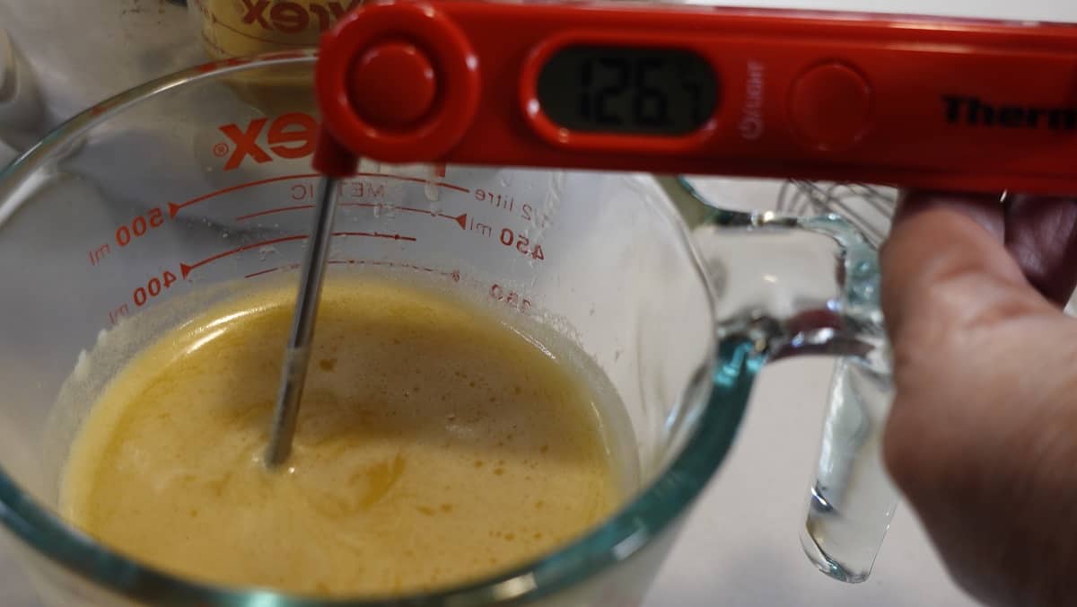 An instant read thermometer in a glass measuring cup with heated apple cider and butter.