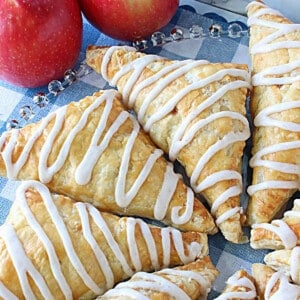 Puff Pastry Apple Turnovers on a glass plate with a confectioners sugar drizzle on each.
