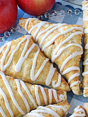 Puff Pastry Apple Turnovers on a glass plate with a confectioners sugar drizzle on each.