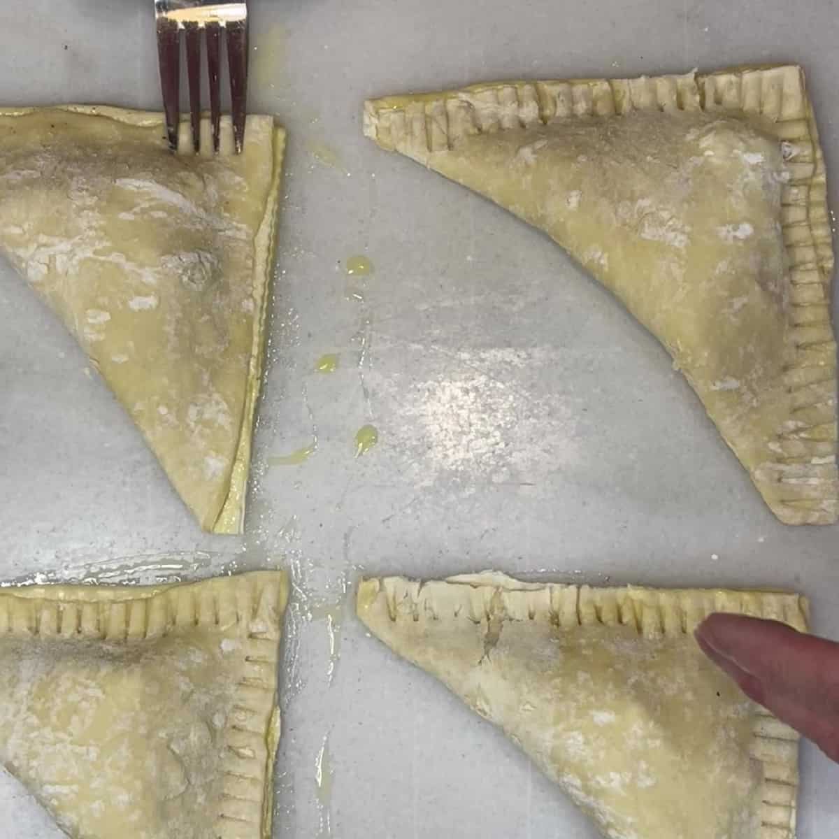 A fork pressing the edges of pastry to make apple turnovers.