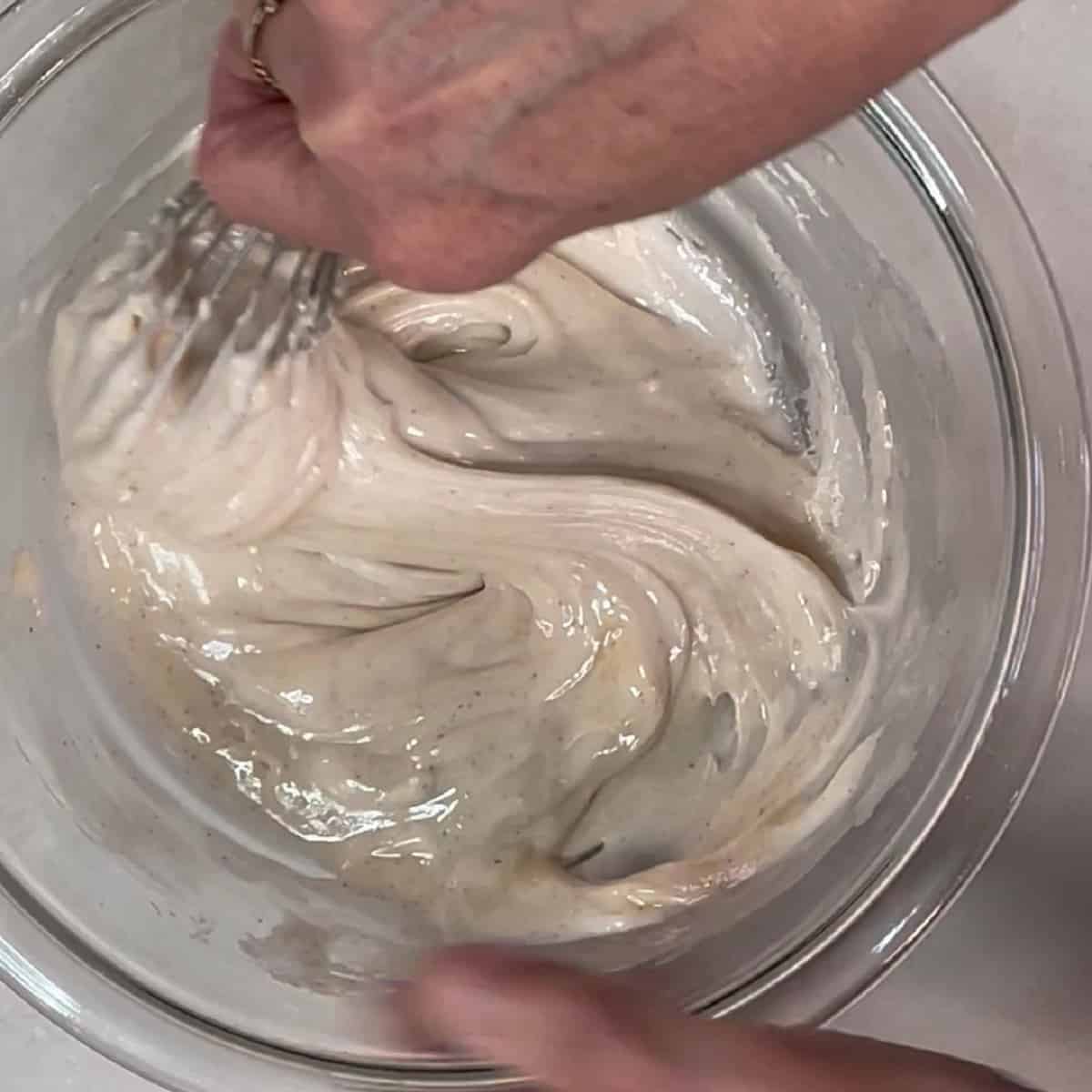 A cinnamon flavored confectioners sugar glaze in a glass bowl with a whisk.