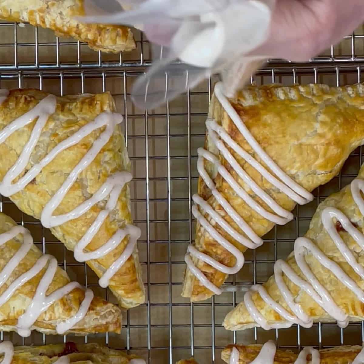 Baked puff pastry apple turnovers getting a zig zag of cinnamon confectioners sugar glaze.