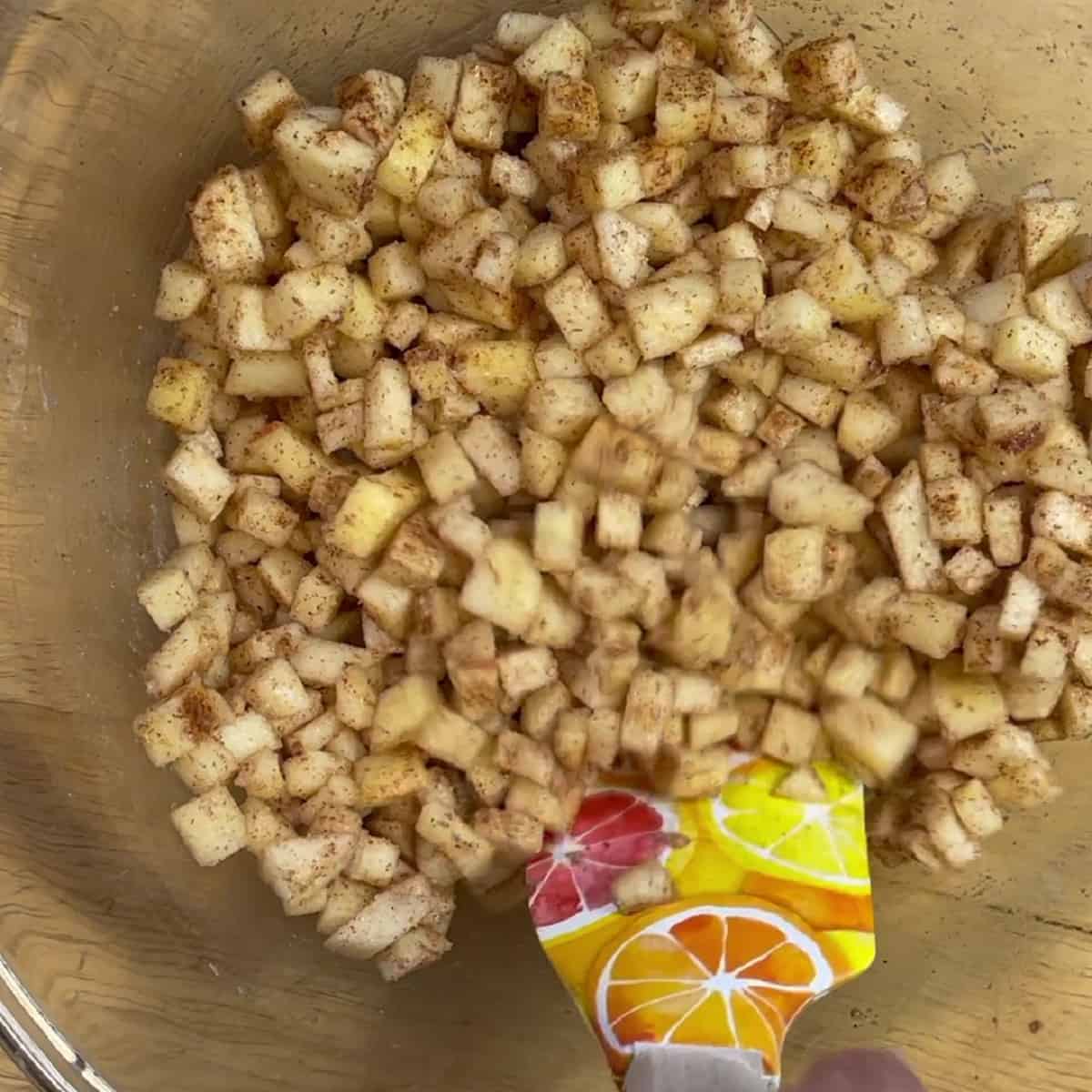 Diced apples mixed with cinnamon and sugar in a bowl with a spatula.