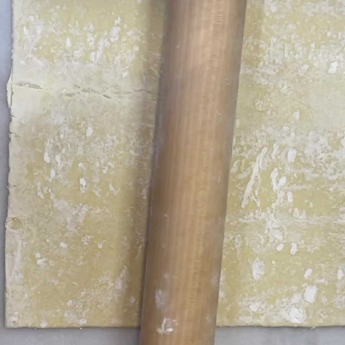 A wooden rolling pin on top of a puff pastry sheet.