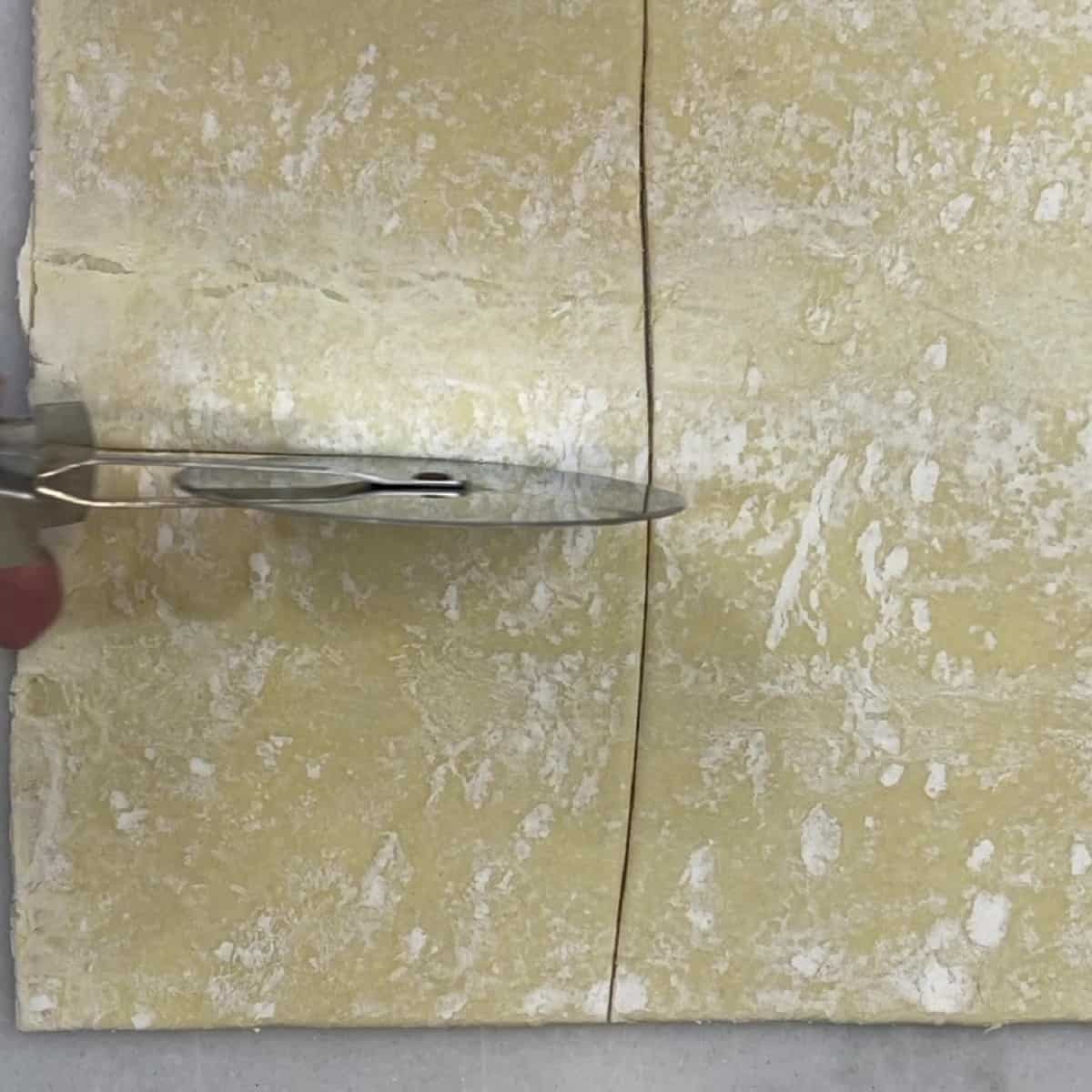 A pizza wheel cutting a puff pastry sheet into four pieces for apple turnovers.