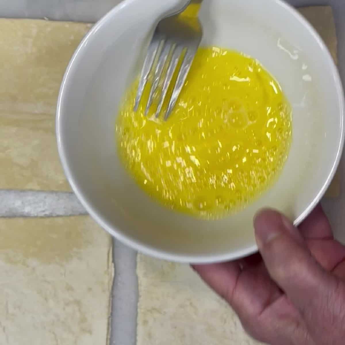 Egg wash in a small bowl with a fork.