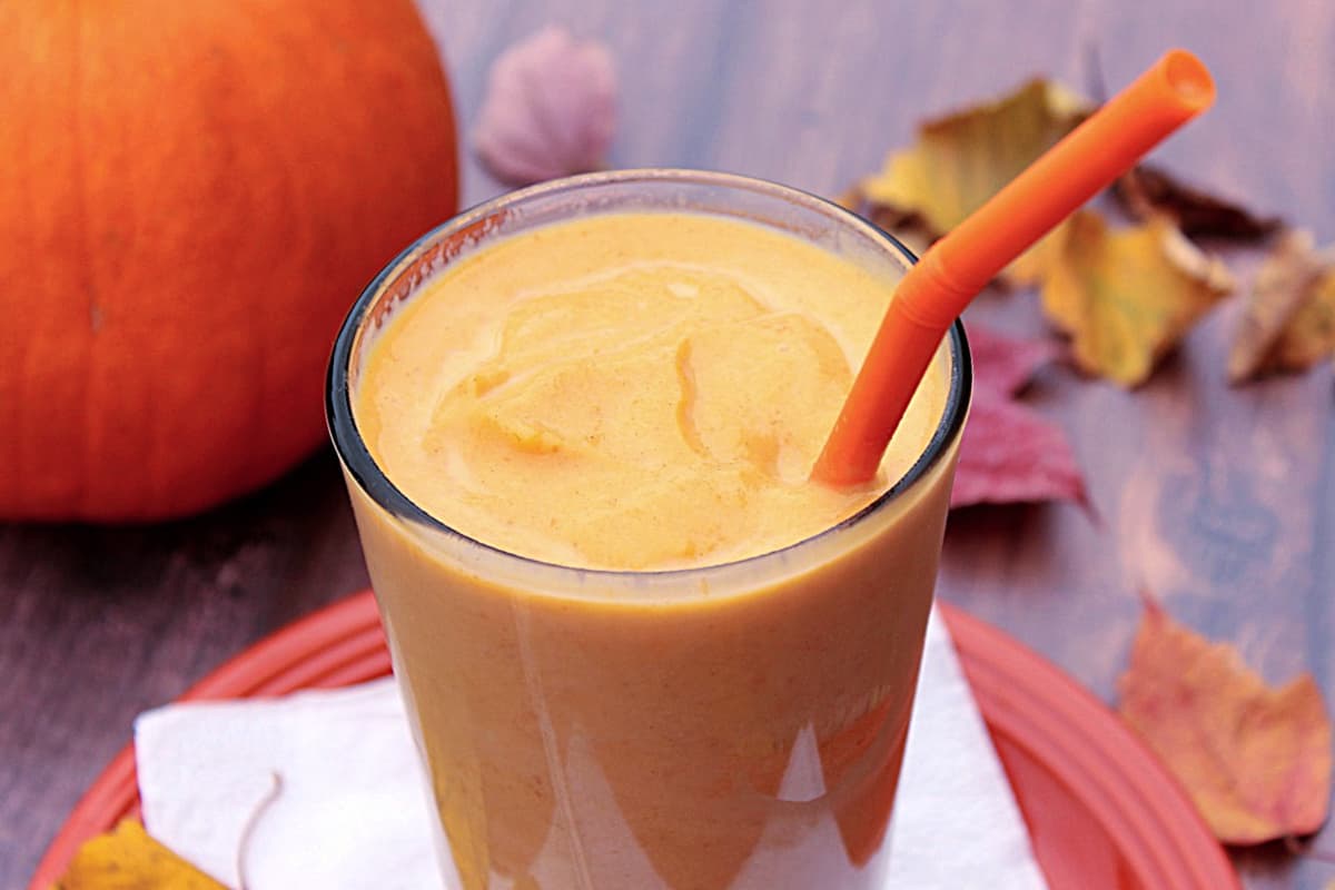 On orange Pumpkin Spice Malted Milkshake in a glass with colorful leaves on the table.