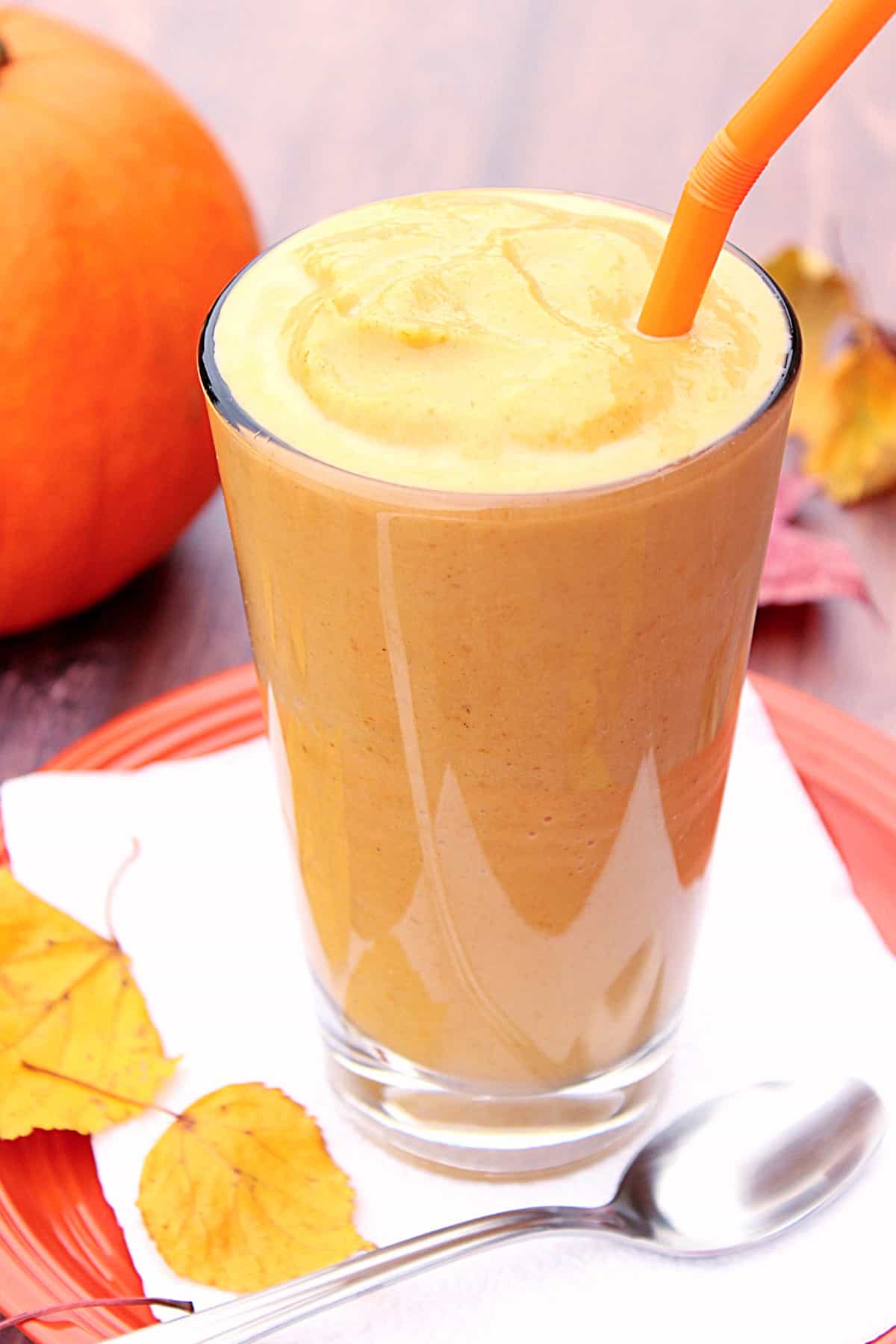 A tall glass filled with a Skinny Pumpkin Spice Malted Milkshake and an orange straw.