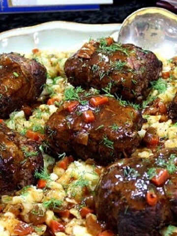 A plate filled with German Beef Rouladen and covered with dark brown gravy.
