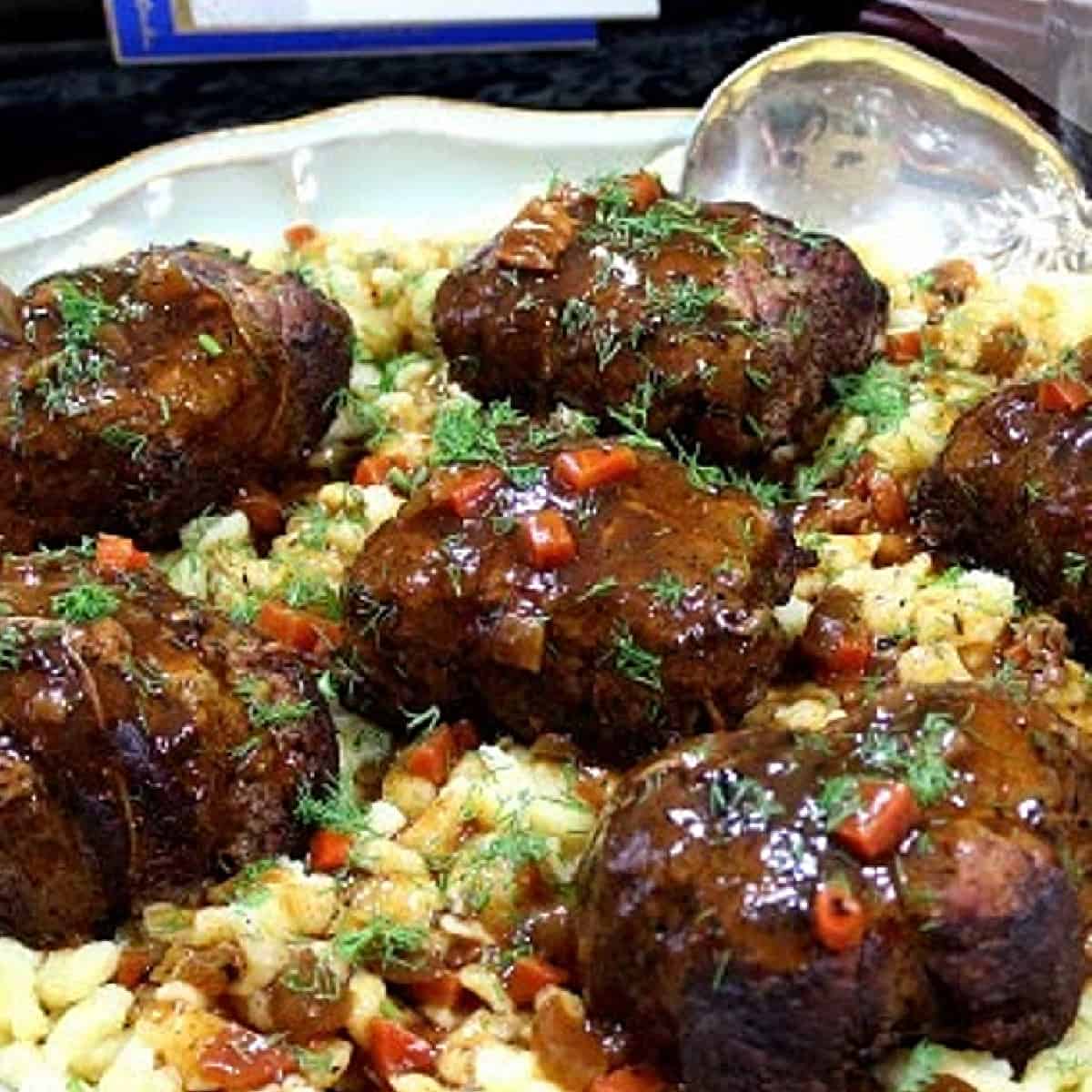 A plate filled with German Beef Rouladen and covered with dark brown gravy.