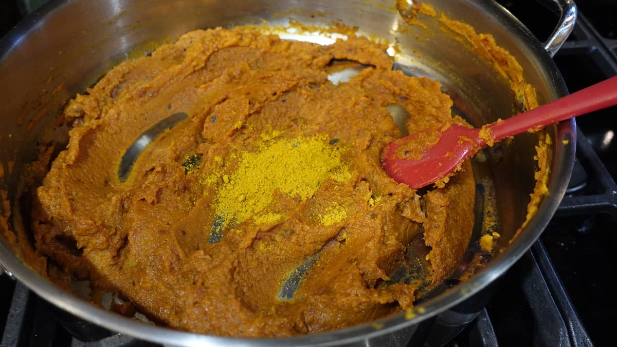Curry powder added to a pumpkin curry sauce in a skillet.