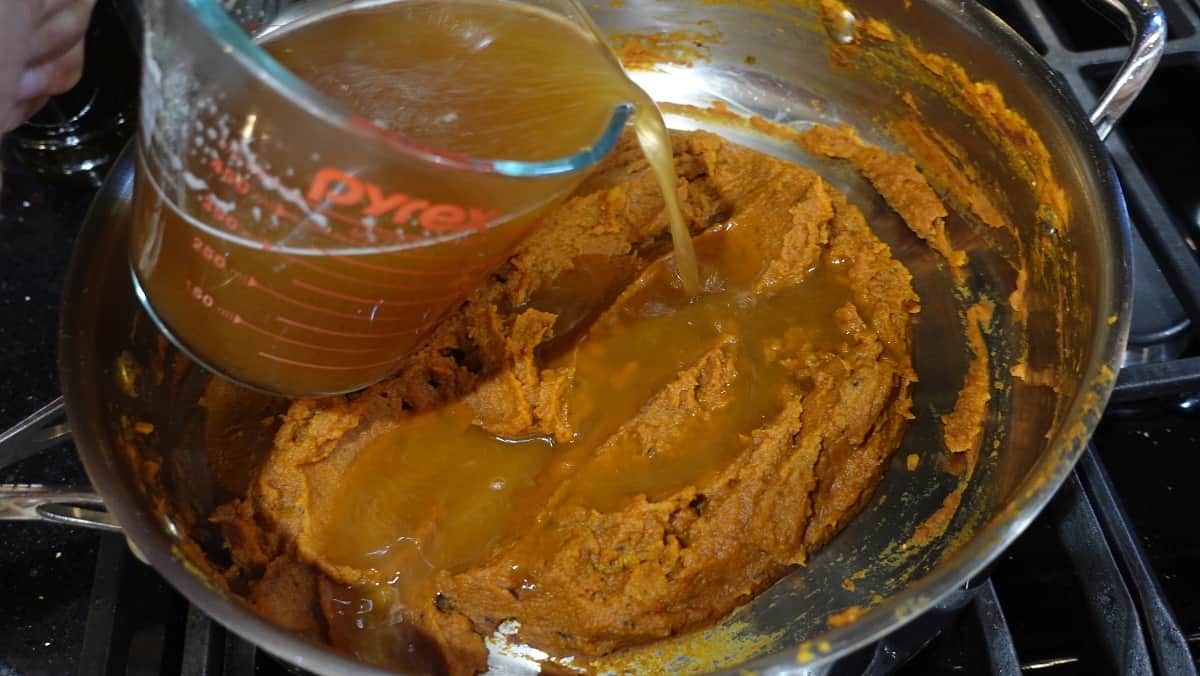 Beef broth being added to a pumpkin curry sauce in a skillet.