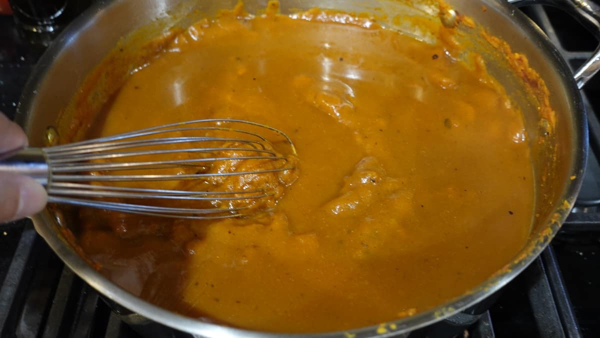 A whisk stirring a skilled filled with pumpkin curry sauce.