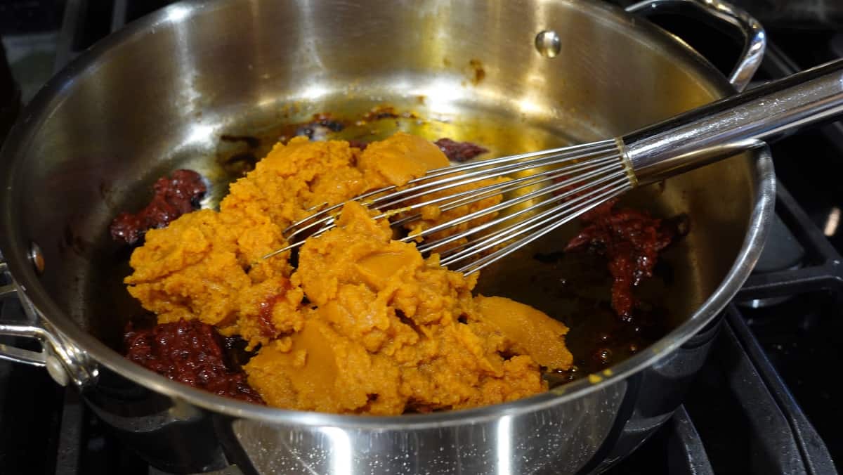 Pumpkin puree being added to a skillet to make a pumpkin curry sauce.