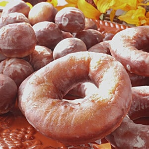 A closeup of a Glazed Apple Cider Donut on an orange platter along with donut holes.