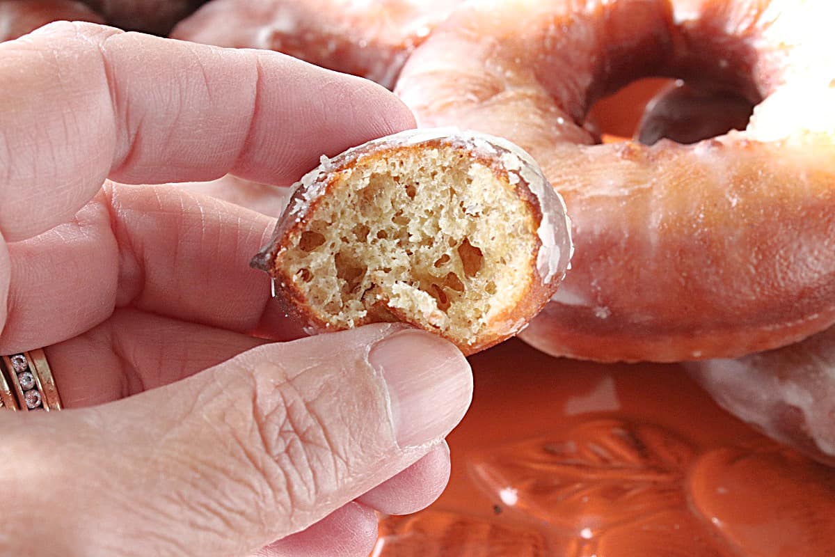 A hand holding a Glazed Apple Cider Donut hole with a bite taken out.