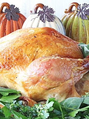 A golden brown Brown Bag Roast Turkey on a platter with fresh herbs.