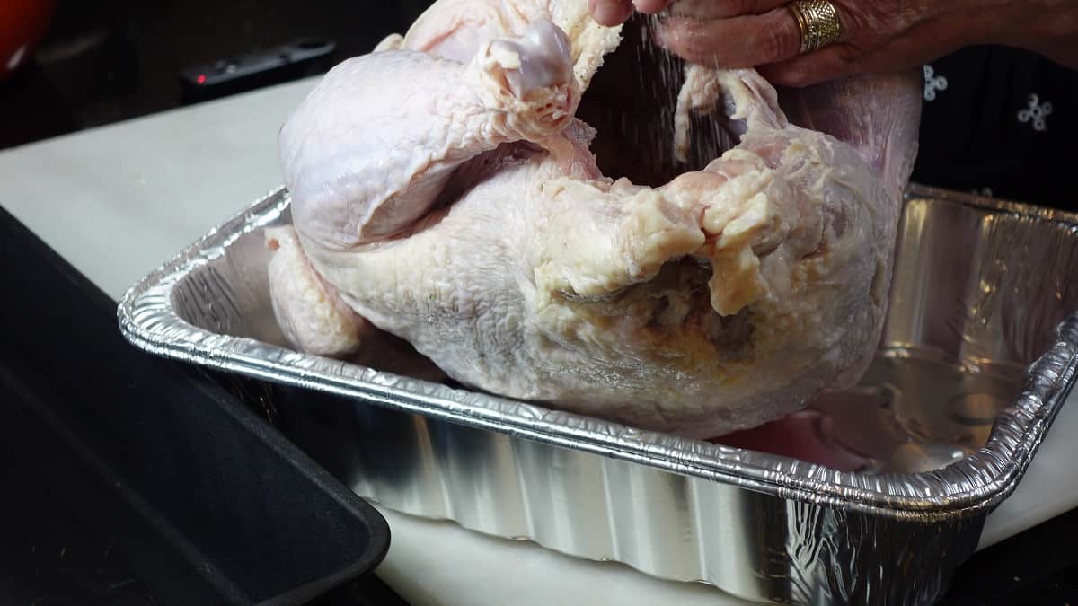 Hand seasoning the inside of a raw whole turkey with salt and pepper.