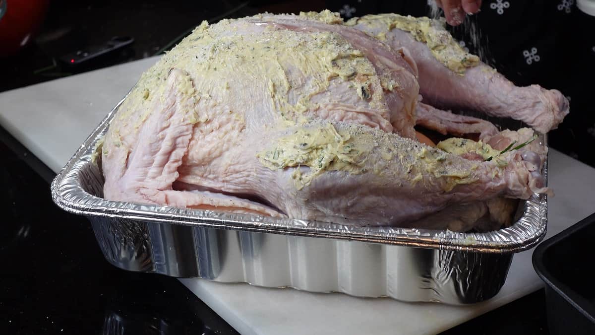 A whole turkey before roasting with a roasted garlic and herb compound butter spread all over the skin.