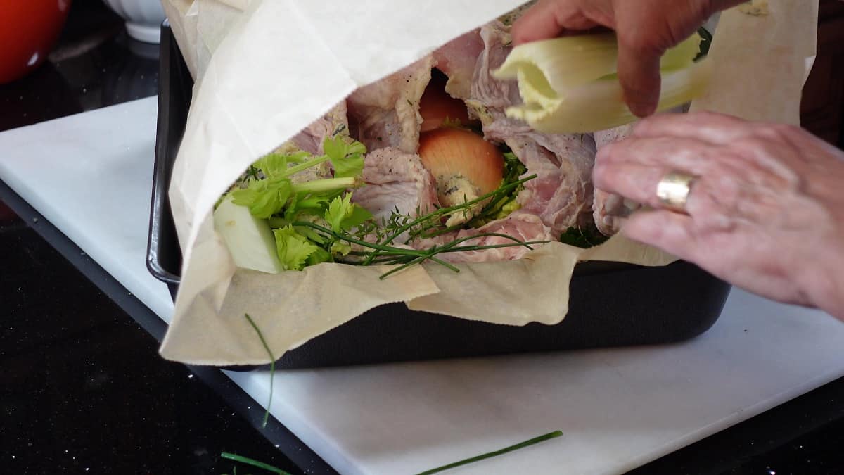 A whole turkey inside a brown parchment paper bag along with vegetables and fresh herbs.