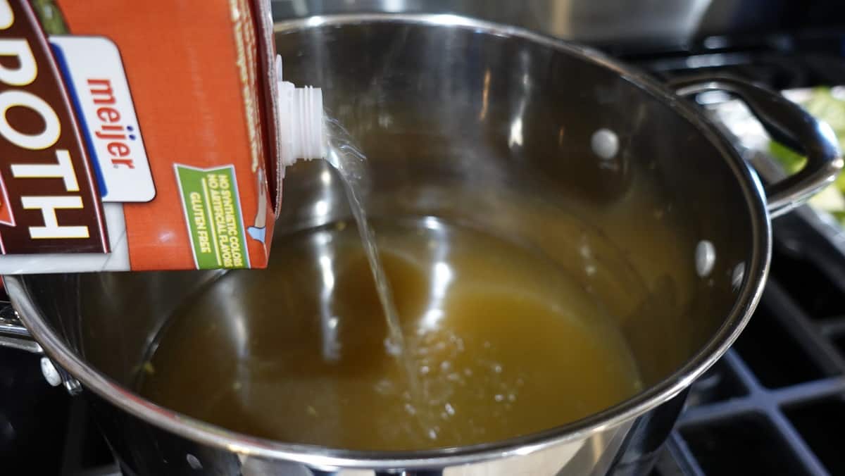 Chicken broth being poured into a saucepan.