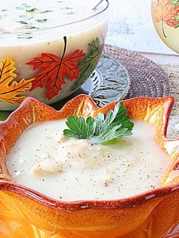 A serving of Creamy Leftover Turkey Soup with Potatoes in a pretty leaf bowl and a parsley sprig.