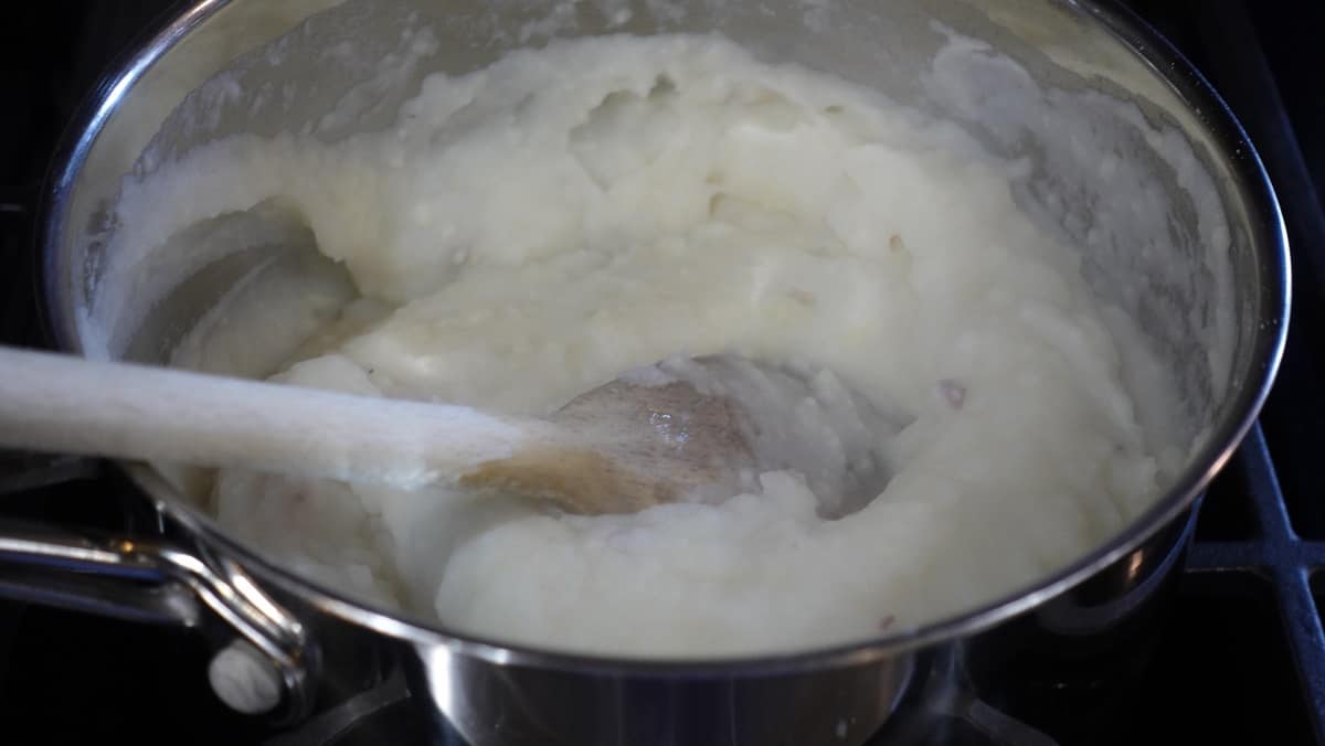 A saucepan filled with mashed potatoes and a wooden spoon.