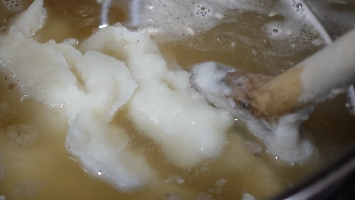 Mashed potatoes being added to a saucepan with chicken stock.