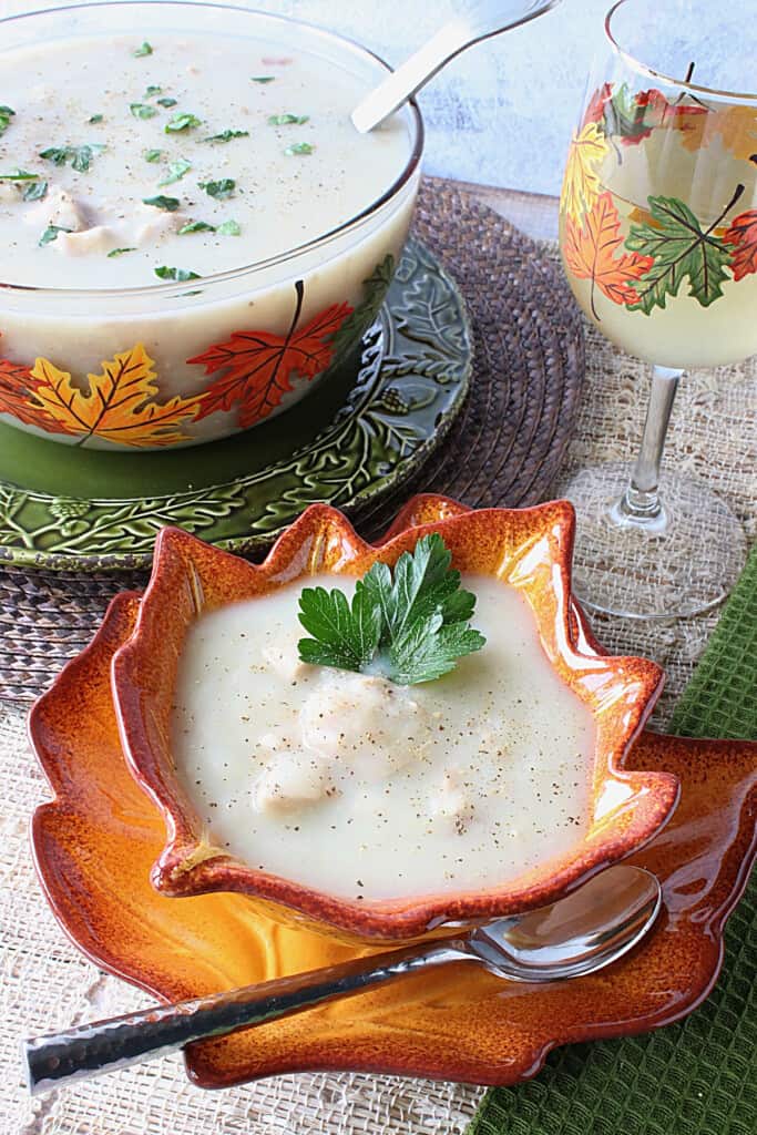 Some creamy turkey potato soup in a bowl with a glass of wine in the background.