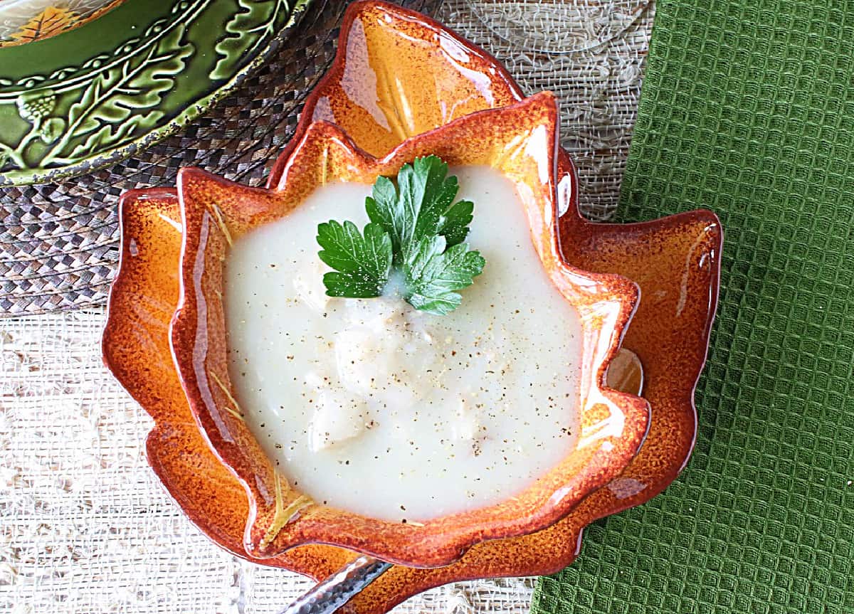 A cute orange leaf bowl filled with Creamy Turkey Potato Soup with black pepper and some parsley.