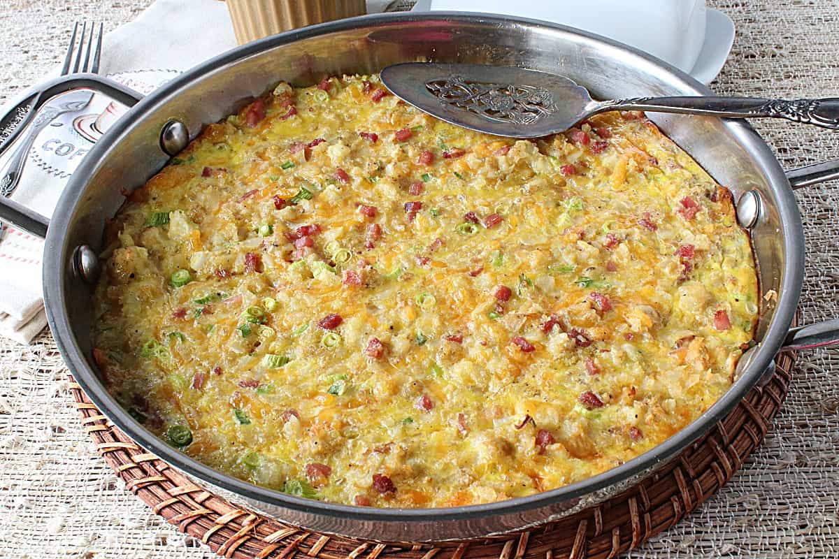 An entire Tater Tot Breakfast Casserole in a silver skillet with a silver spatula on tip.