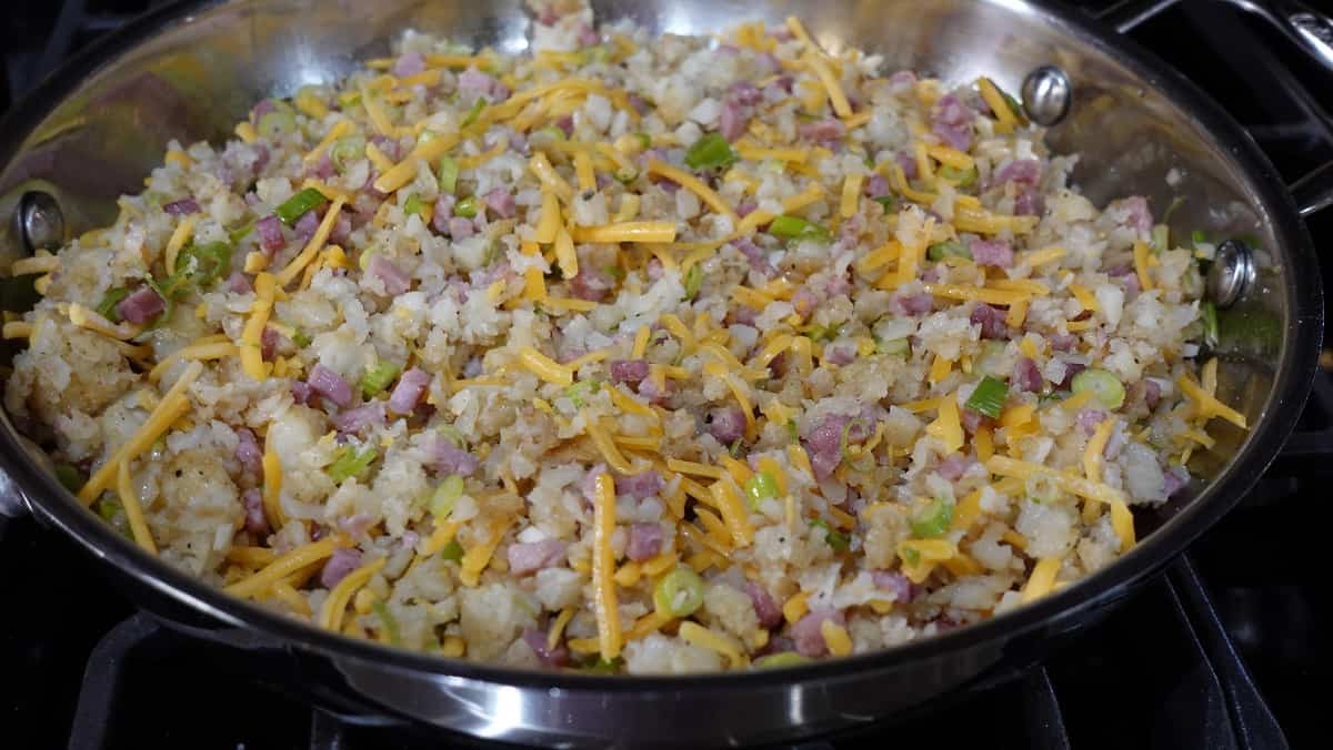 Broken tater tots, ham, cheese, and scallions in a skillet.