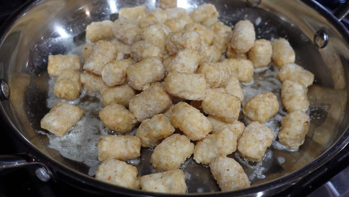 Tater tots in a skillet with melted butter.