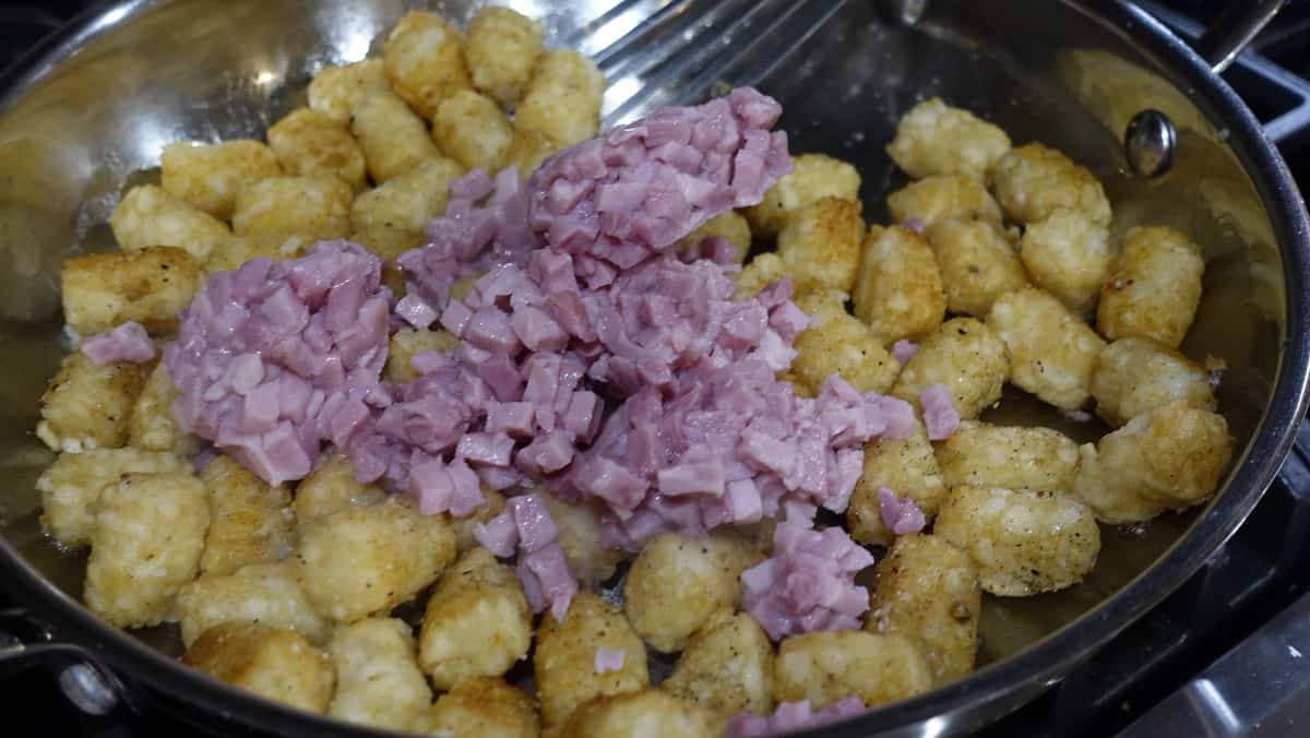 Diced ham and tater tots in a skillet on the stove.
